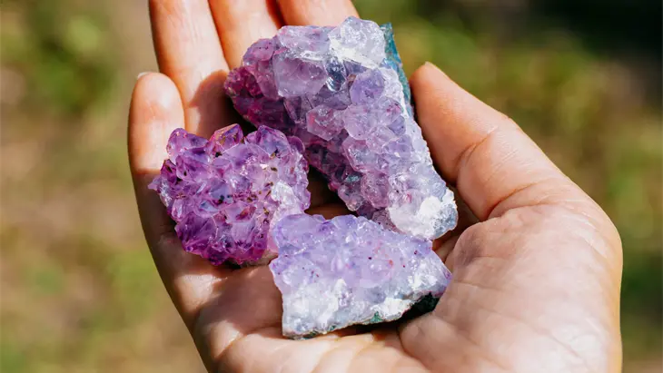 Eine offene Hand, die drei Stücke glitzernden, violetten Amethyst hält.