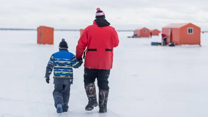Un padre y su hijo caminan por el congelado lago Simcoe hacia cabañas de pesca en el hielo en un soleado día de invierno.
