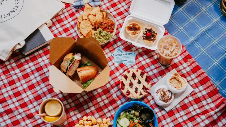 Eine Pastete, ein Sandwich, Getränke und andere Picknick-Speisen auf einer rot karierten Decke vom Savour and Sip Trail in Stratford, Ontario.