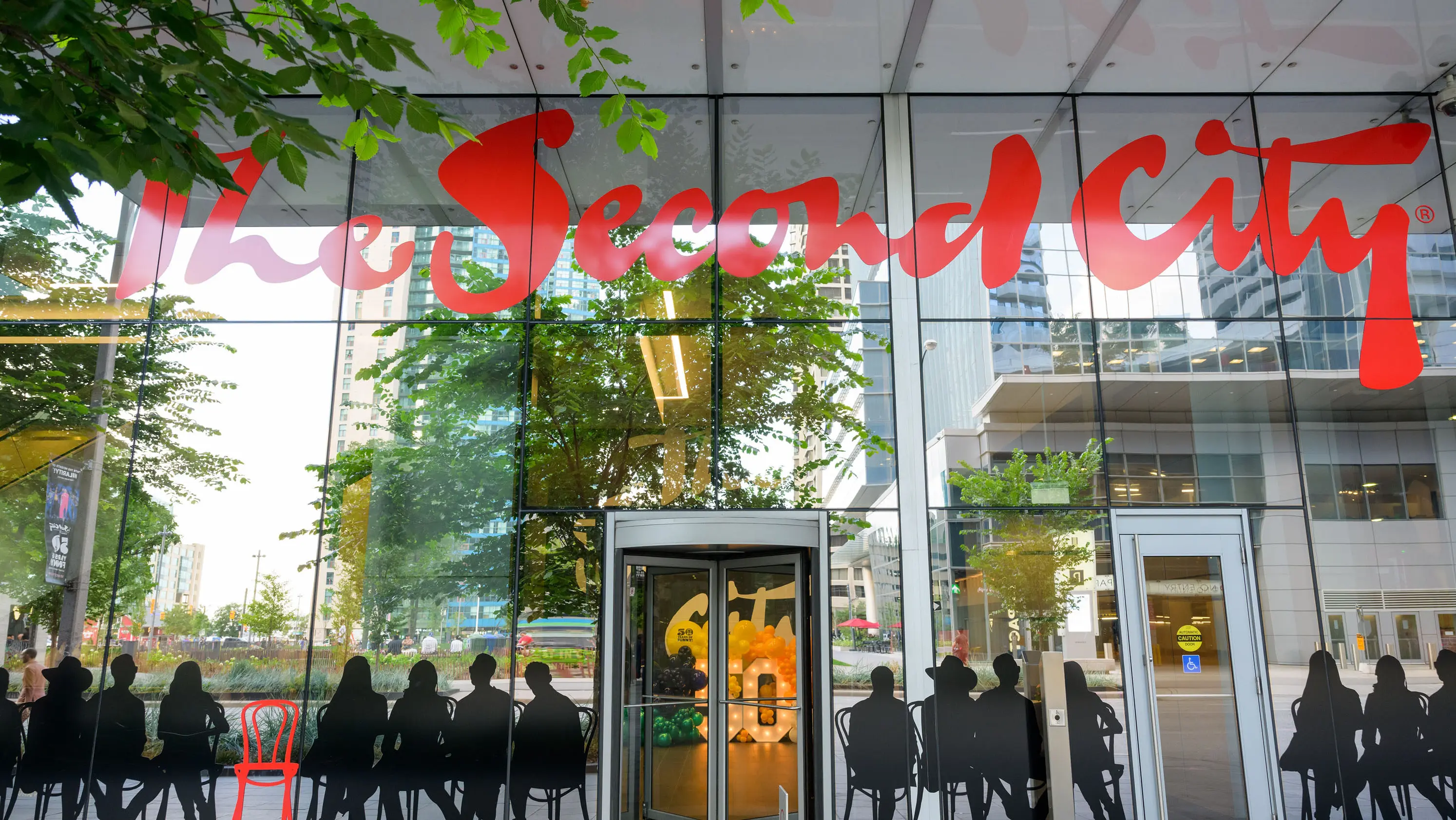 온타리오 주 토론토에 있는 세컨드 시티 코미디 클럽의 입구. 유리창에 굵은 빨간색 글씨가 쓰여 있고, 앉아 있는 사람들의 실루엣이 특징입니다.