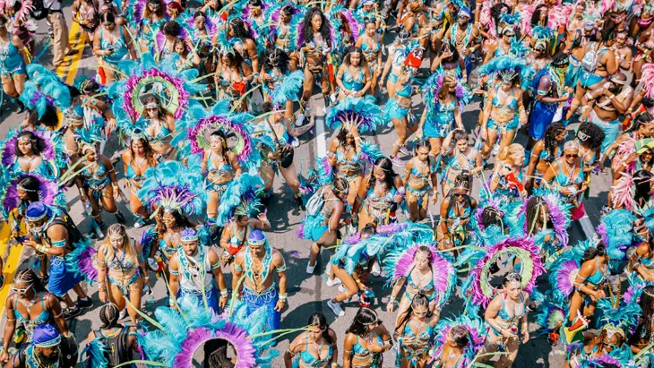 Luftaufnahme einer Parade während des Toronto Caribbean Carnival mit in Blau, Lila und Grün gekleideten und mit Federn geschmückten Darstellern.