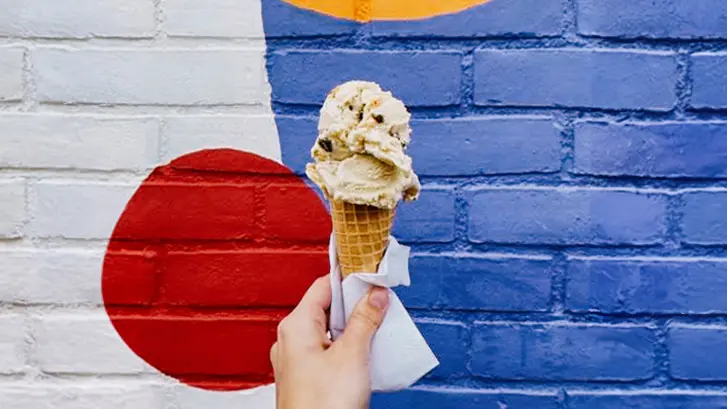 Close-up of a hand holding an ice cream cone in front of Flurple’s.
