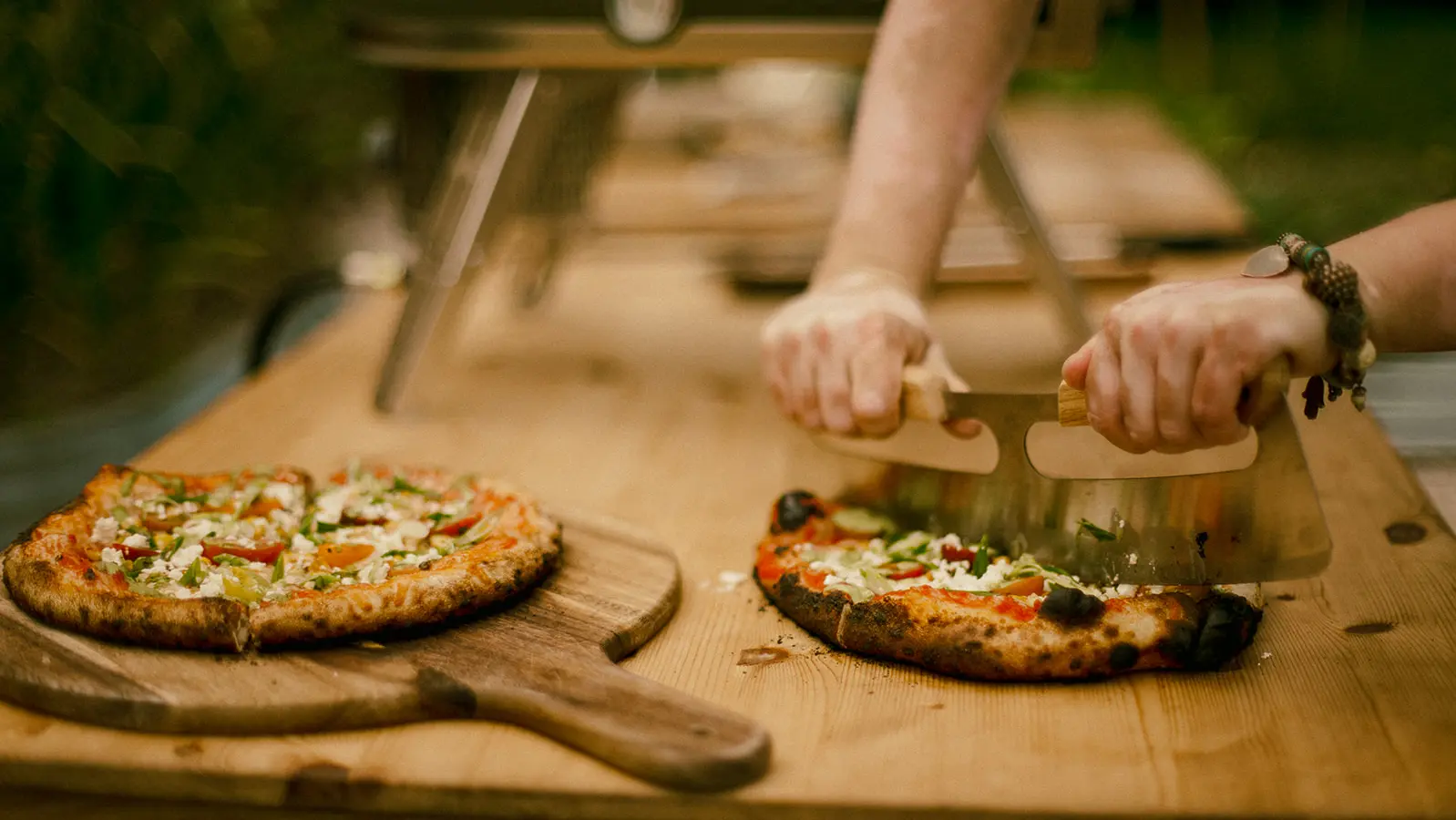 갓 구운 장작불 피자 두 장이 나무판 위에 놓여 있습니다. 한 피자는 메짜루나로 자르고 있습니다.