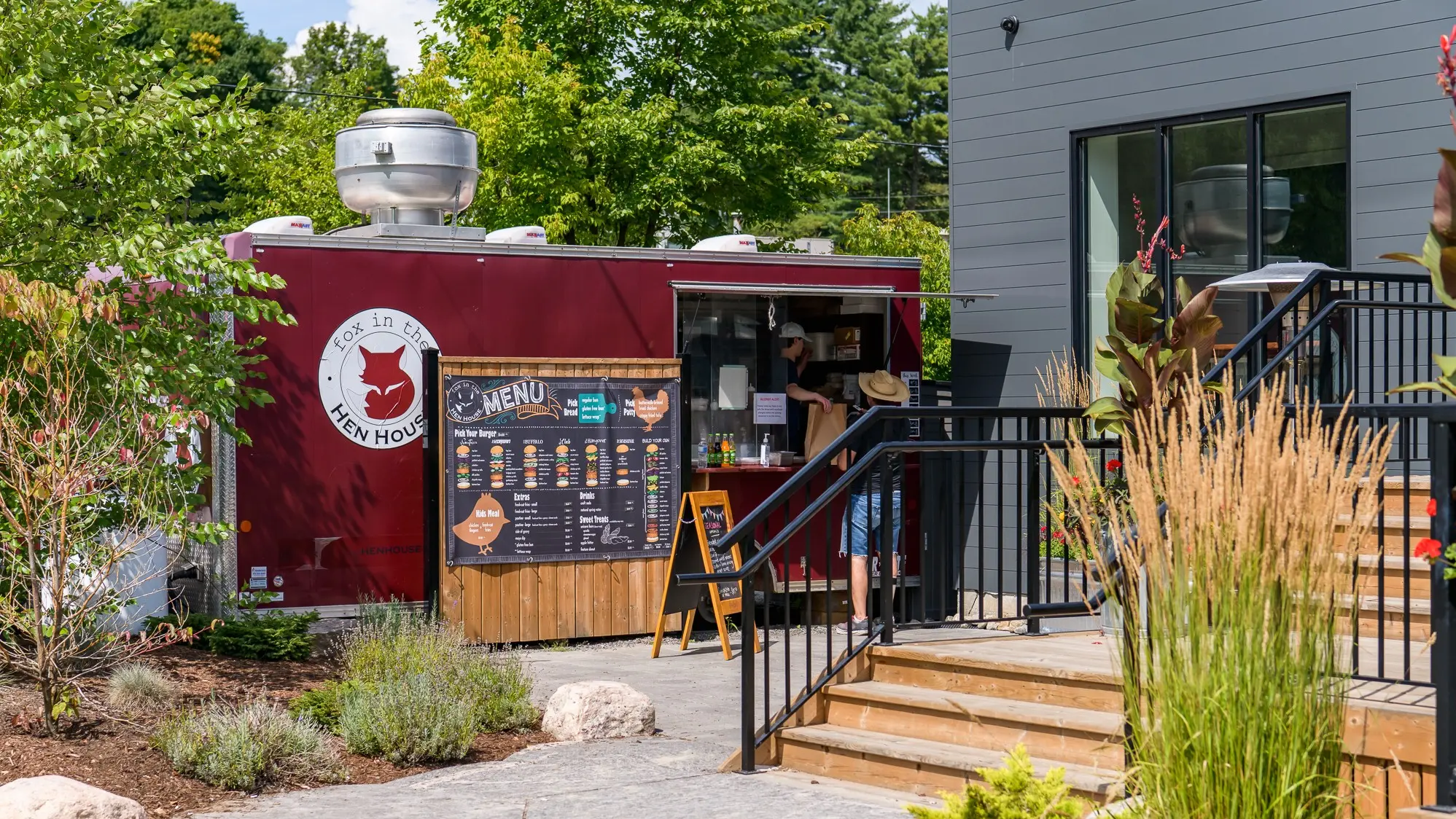 Exterior of the red, Fox in the Hen House food truck surrounded by lush trees.