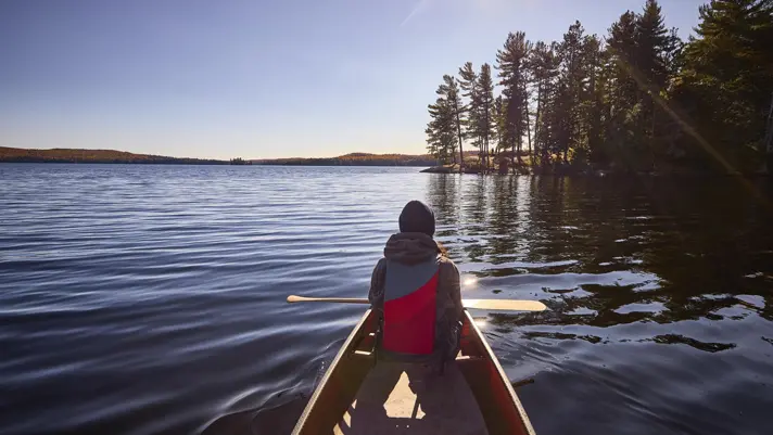 View of a paddler in the front of a canoe on the calm waters of Opeongo Lake in Algonquin Park.