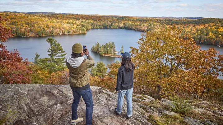 Un couple admire la vue sur les couleurs d'automne de la forêt depuis le belvédère du lac Spectacle dans les hautes terres de l'Ontario.