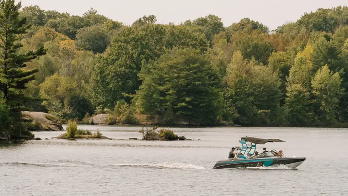 Ein Boot fährt an einem bewaldeten Ufer eines Sees in Muskoka vorbei.