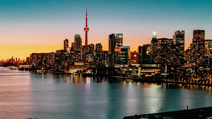 Skyline von Toronto mit leuchtenden Gebäuden bei Nacht, unter einem blau-rosa Sonnenuntergang.