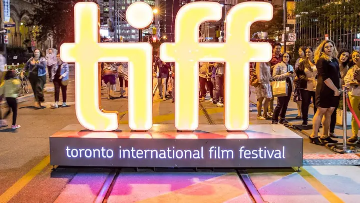 Un gran cartel de neón de TIFF se encuentra afuera de un teatro con una multitud de espectadores durante el Festival Internacional de Cine de Toronto.