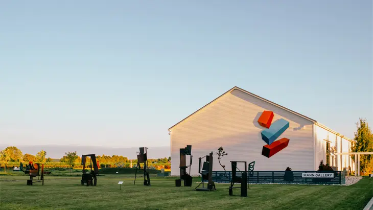 Eine weiße Scheune auf einem flachen, grünen Weingut unter einem klaren blauen Himmel.