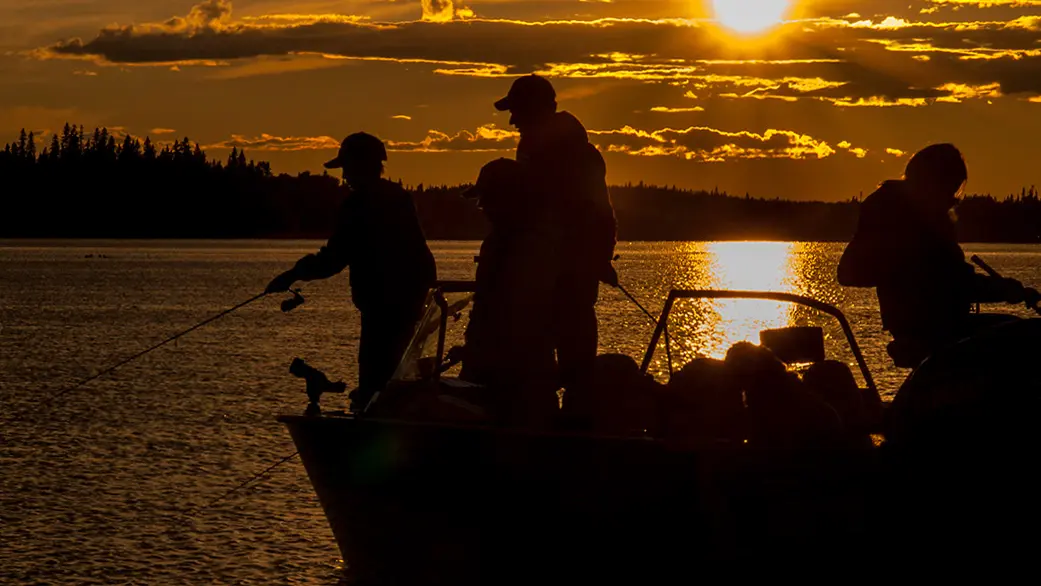 Drei Personen angeln bei Sonnenuntergang von einem Boot im Fushimi Provincial Park.