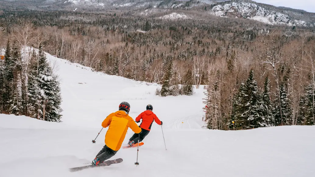 Zwei alpine Skifahrer genießen ihre Abfahrt auf einer verschneiten Piste im Searchmont Resort in der Nähe von Sault Ste. Marie.