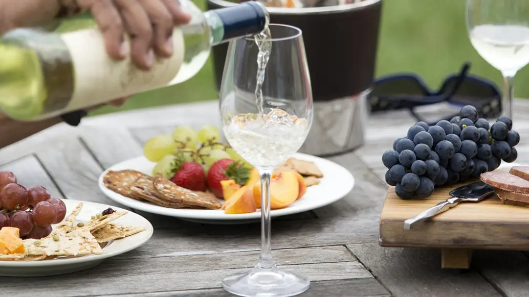 A person pours a glass of white wine to accompany an outdoor picnic with fruit and cheese at Viewpoint Estate Winery.