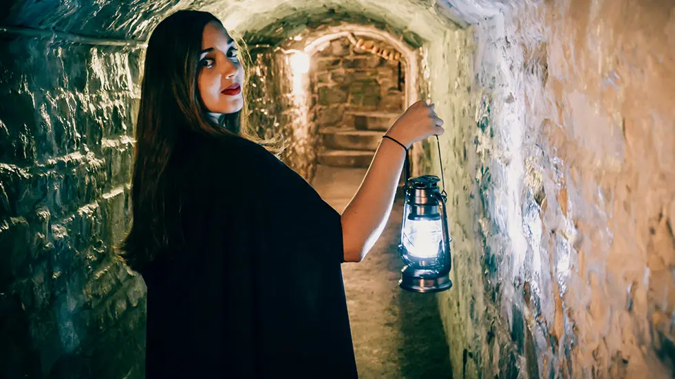 A woman leads a haunted walk, glancing over her shoulder as she enters a dark tunnel.