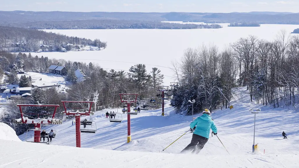青い冬用コートを着たアルペンスキーヤーが、マスコーカのヒドゥンバレーにあるスキーコースを滑降している。