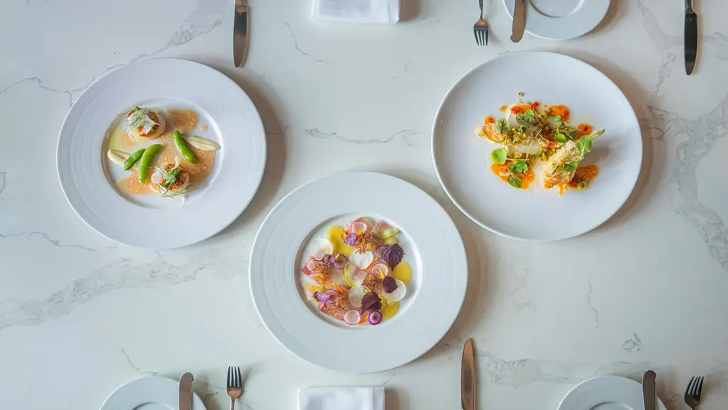 A beautifully set table with three appetizing meals served on white dishware and a linen tablecloth at an upscale restaurant.
