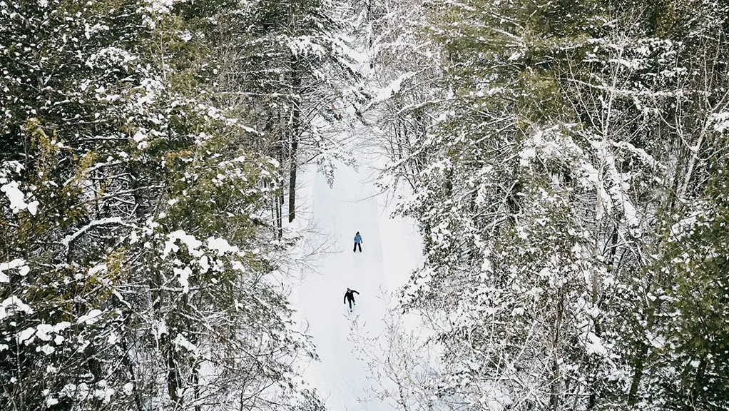 Vue aérienne montrant deux personnes patinant sur un sentier de patinage bien entretenu dans la forêt du parc Arrowhead