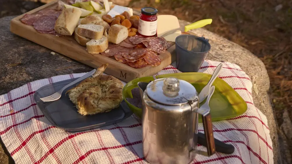 Una pareja se sienta en un banco de troncos frente a un fuego rugiente en un campamento con vista a un gran lago.