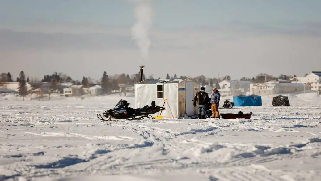 Des pêcheurs sur glace se tiennent à côté d'une motoneige et d'une cabane de pêche sur glace sur un lac gelé lors du Wawa Ice Fishing Derby.