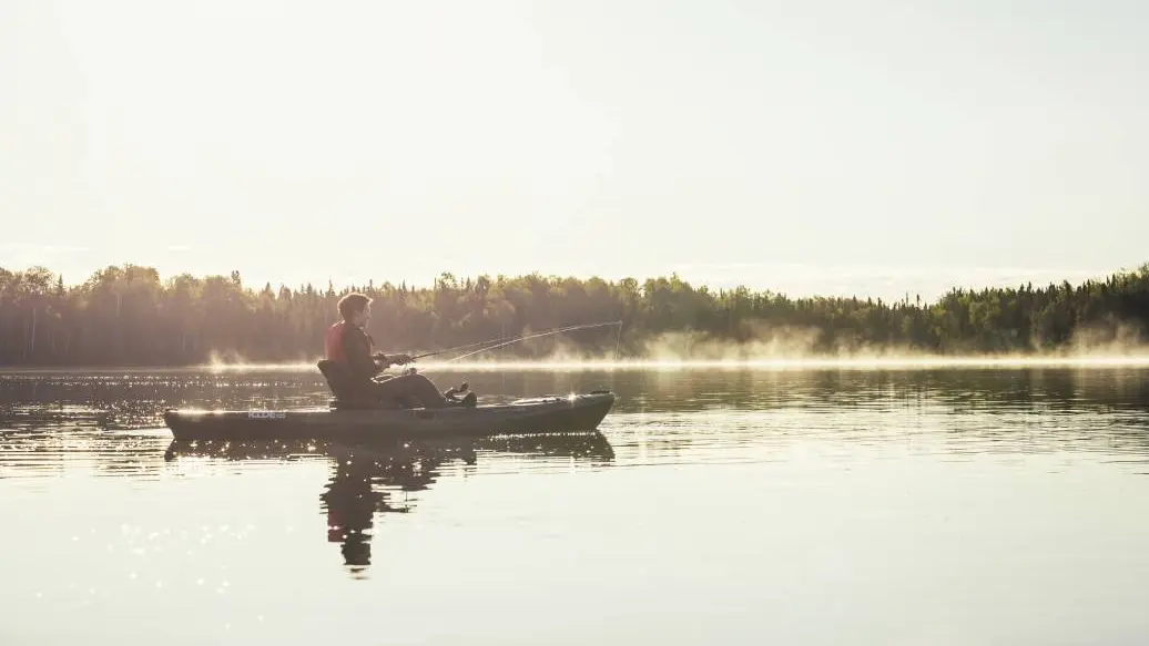 An angler fishing from a kayak in a misty lake in Northwest Ontario.