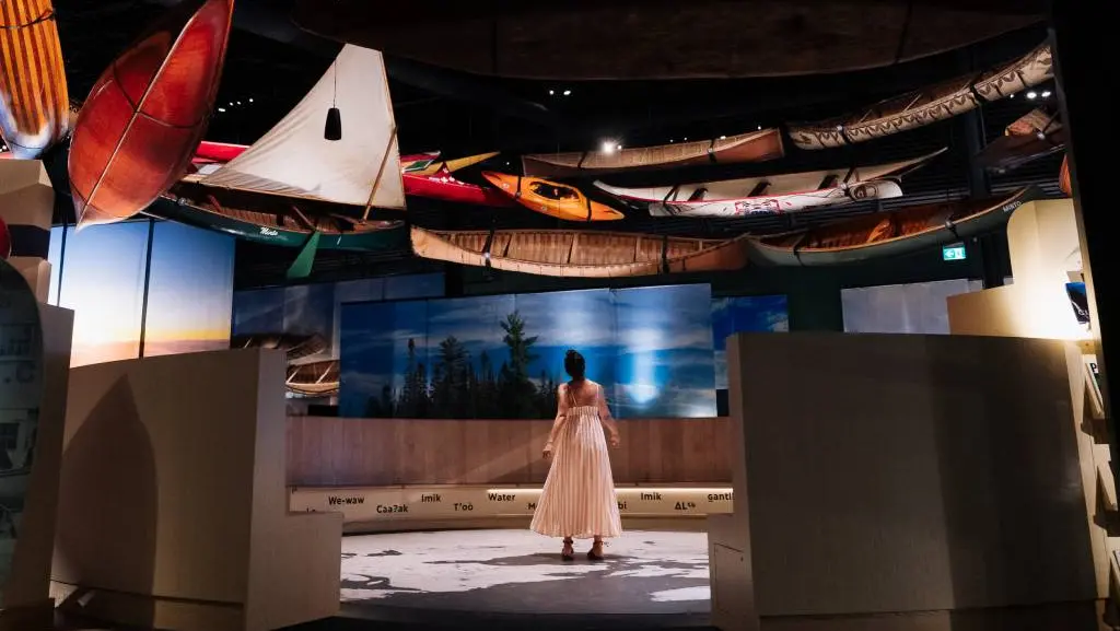 한 여성이 캐나다 카누 박물관의 비공개 투어에 참여하여 전통 카누와 카약을 포함한 다양한 수상 운송 수단들을 둘러보고 있다.
