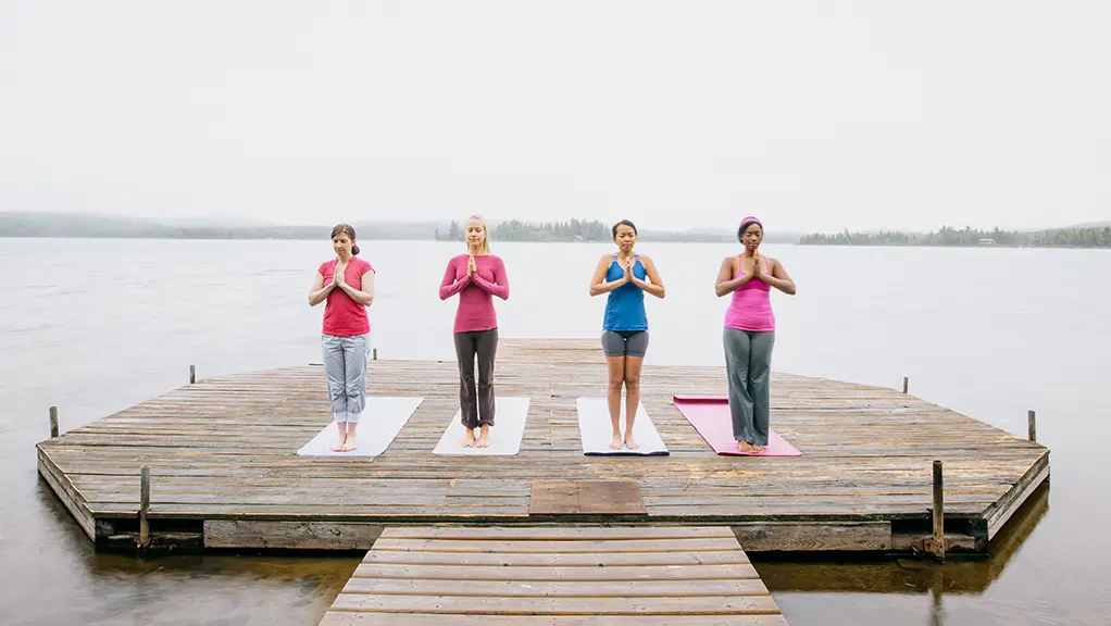 Group of people meditating on a wooden dock overlooking a calm lake.