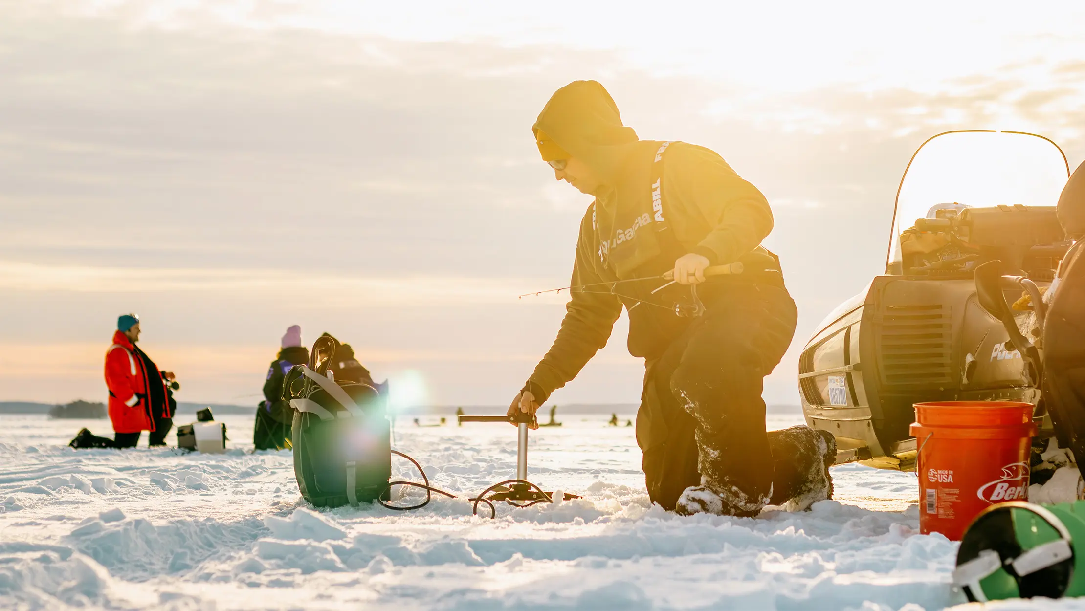 People preparing ice fishing gear on a frozen lake at sunrise.