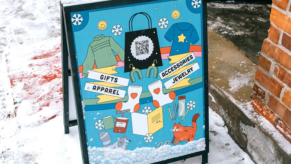 Letrero ilustrado para acera que promociona tiendas y eventos locales, ubicado en una acera nevada.