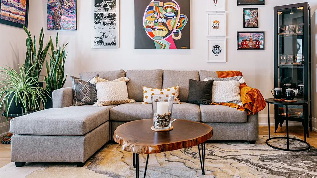 Salon moderne avec canapé d’angle, table basse et œuvres d’art colorées accrochées aux murs.