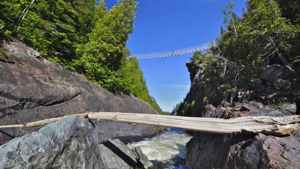 Unos excursionistas cruzan un puente colgante peatonal situado a gran altura sobre las aguas turbulentas a lo largo de una ruta de senderismo en el Parque Nacional de Pukaskwa.