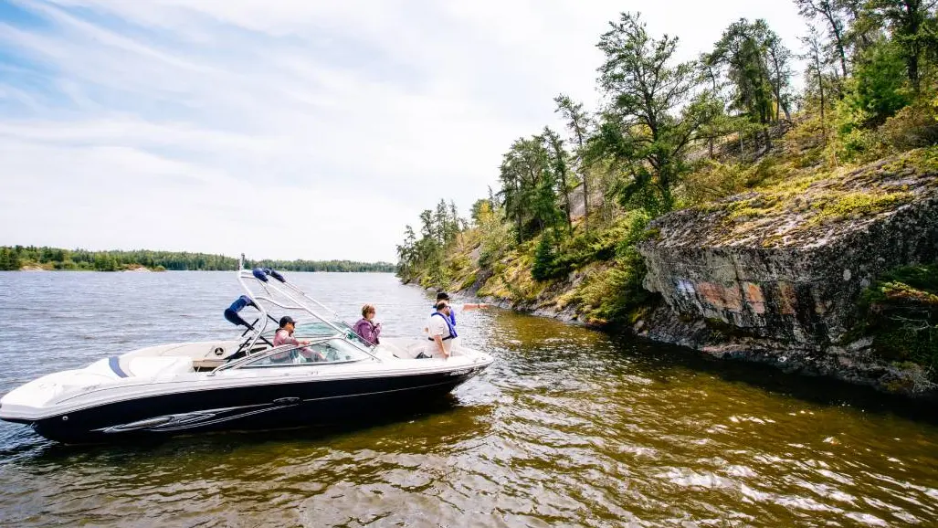 Four people in a speedboat admire unique rock formations along the shoreline of Lake of the Woods.