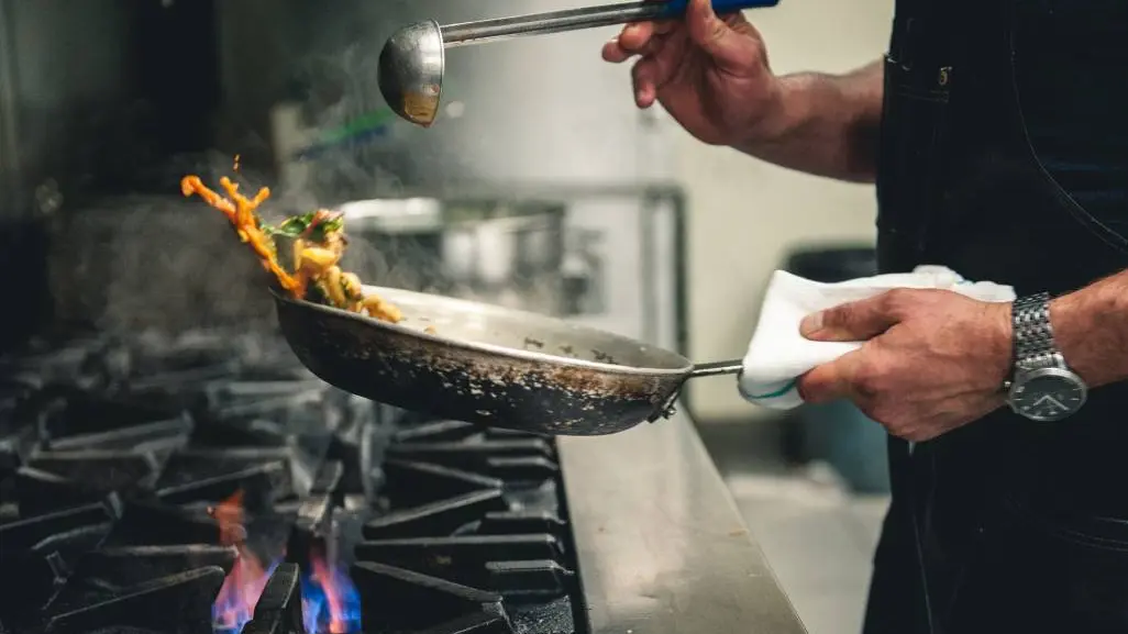 Un chef est en train de faire frire des aliments à la poêle sur une flamme nue dans le restaurant Craft Farmacy.