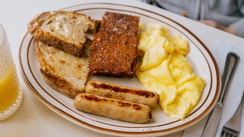 Assiette de brunch composée d’œufs brouillés, de saucisses et de pain grillé, accompagnée d’un verre de jus d’orange.