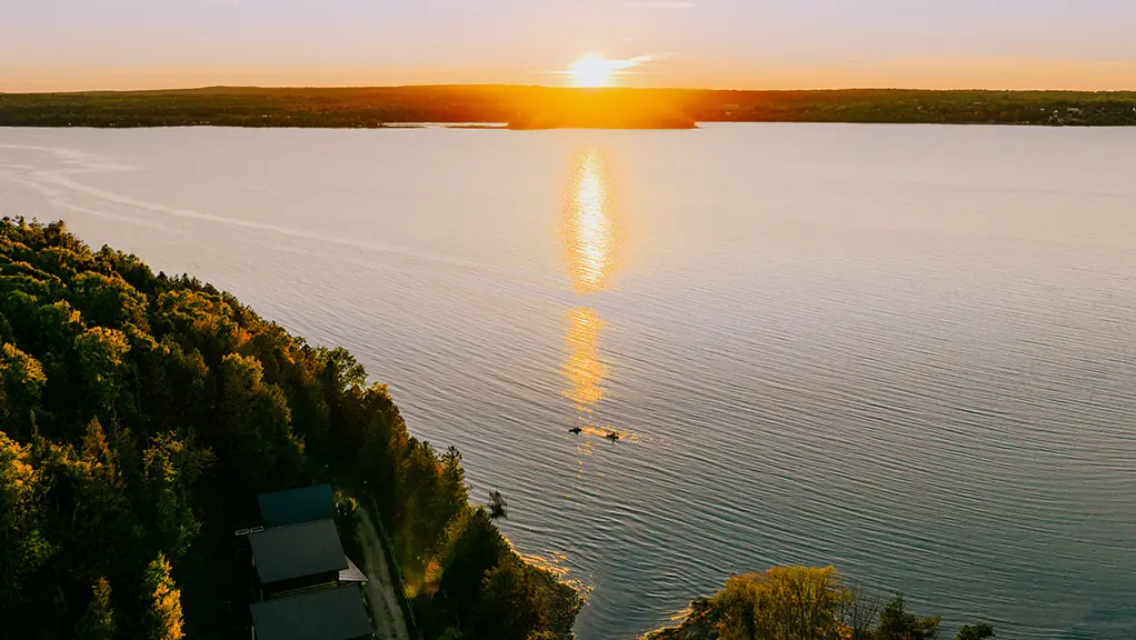 Aerial view of sunset over a lake with forested shoreline.