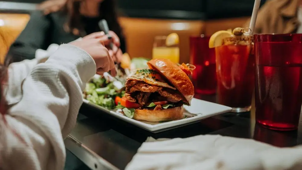 Una jugosa hamburguesa con muchos ingredientes adicionales, servida con ensalada y una bebida afrutada.