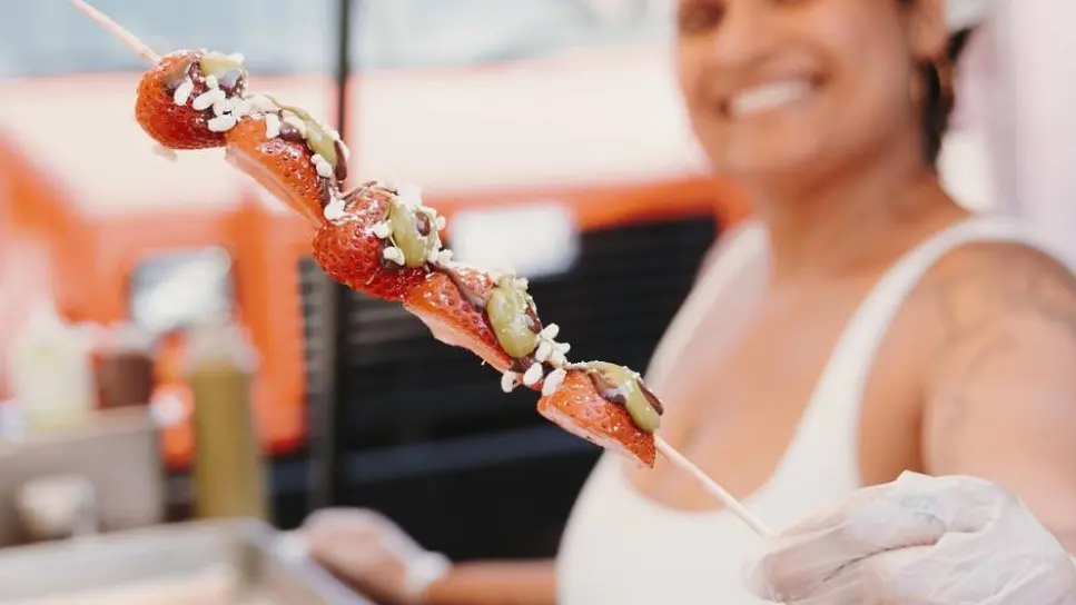 Eine Frau, die an einem Imbissstand arbeitet, bietet auf einem Open-Air-Food-Festival in Toronto einen süß-herzhaften Spieß an.