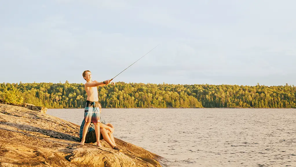 A young boy casts a fishing line from a rocky shoreline in Quetico Provincial Park.
