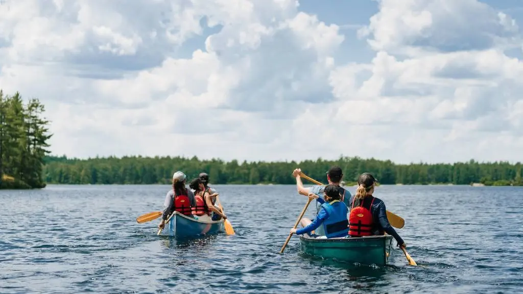 A group of six people paddles in two canoes across a calm lake in Kawartha Highlands Provincial Park.