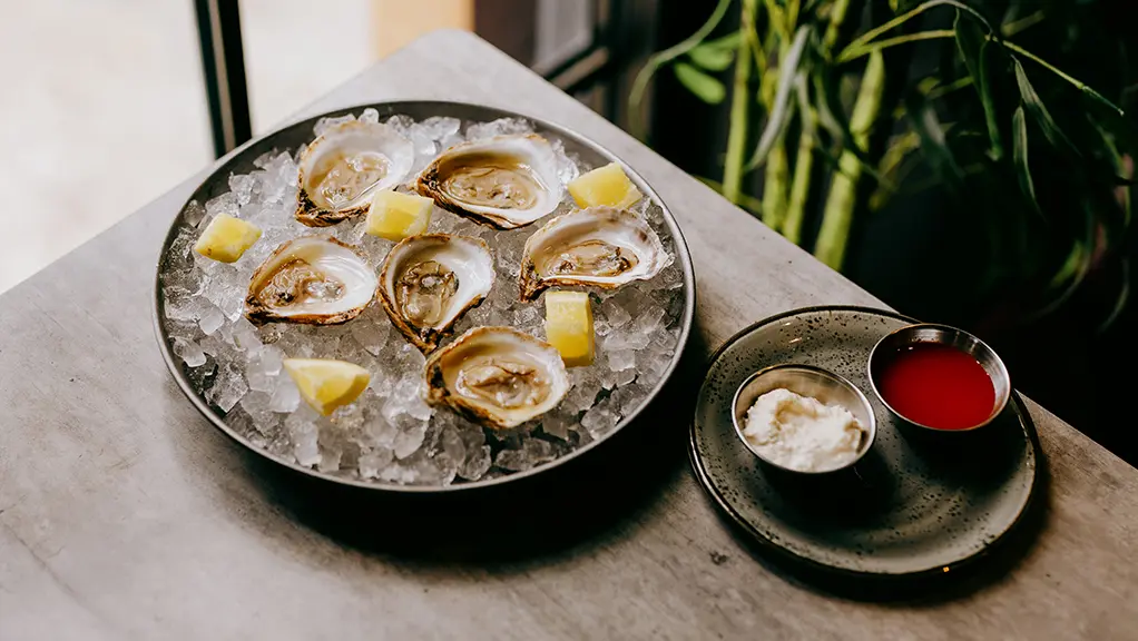 Ostras frescas servidas sobre hielo con rodajas de limón y salsas para mojar en el restaurante Hunter &amp; Co.