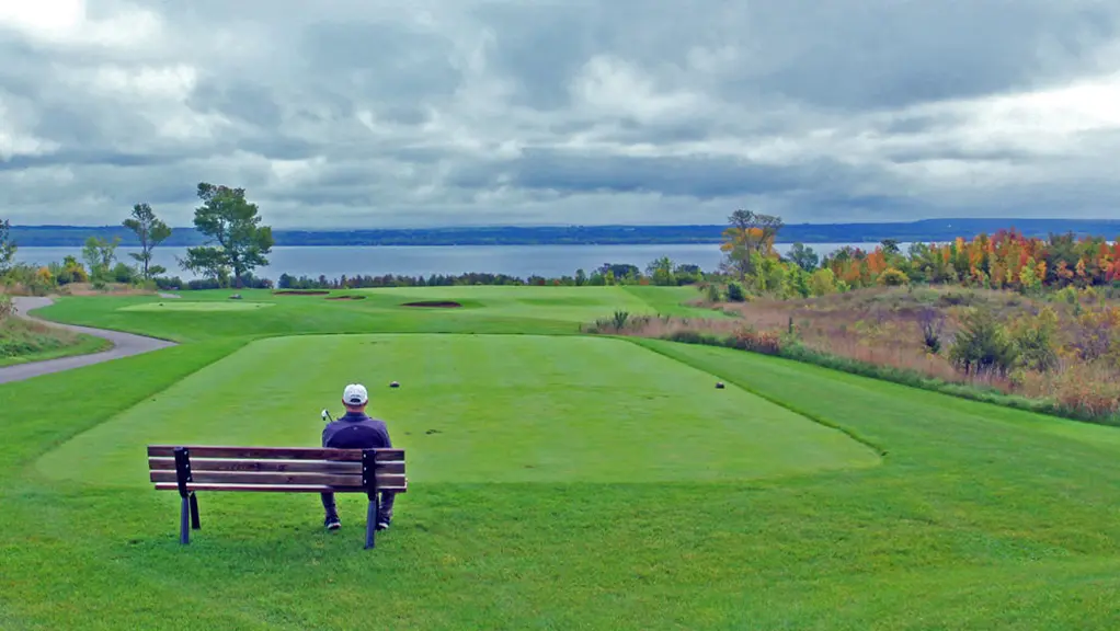 Un homme est assis sur un banc donnant sur un terrain de golf.