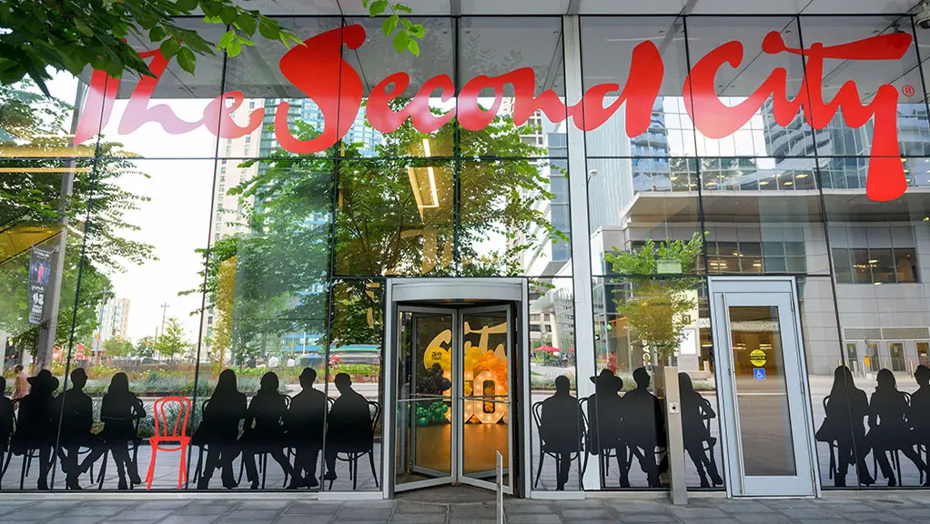La entrada al club de comedia The Second City en Toronto, Ontario, con llamativas letras rojas en el cristal y siluetas de figuras sentadas.