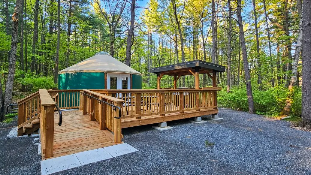Eine runde Jurte als Campingunterkunft mit barrierefreier Holzrampe, Außenterrasse und Sitzbereich im Bon Echo Provincial Park.