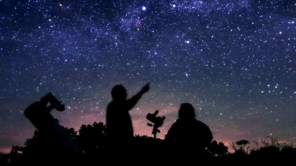 Silhouette von zwei Personen, die auf die Sterne zeigen und zu ihnen hinaufschauen.