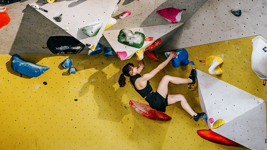 A person climbing an indoor rock-climbing wall with colourful holds.