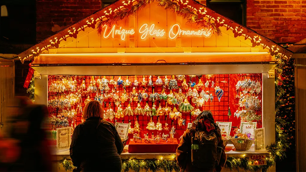 Festive Christmas market stall decorated with garlands and colourful holiday ornaments at night.