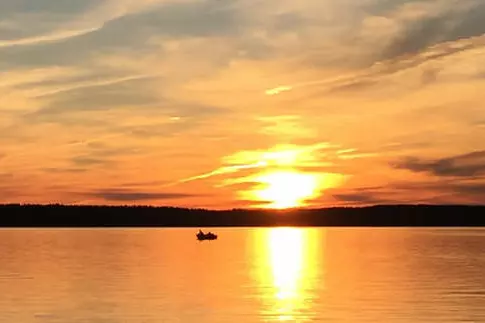 Zwei Angler in einem Boot auf einem großen See unter dramatischem Himmel bei Sonnenuntergang