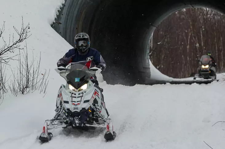 Two snowmobilers riding through a round tunnel.
