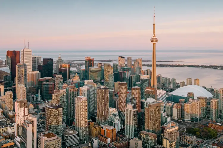 Wolkenkratzer und der CN Tower sind im Licht des Sonnenuntergangs getaucht und blicken auf ruhige Gewässer unter einem sanften, pastellfarbenen Himmel.