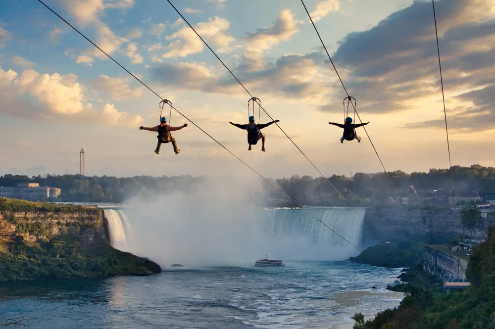 Three people experience a thrilling zipline ride in front of Niagara Falls.