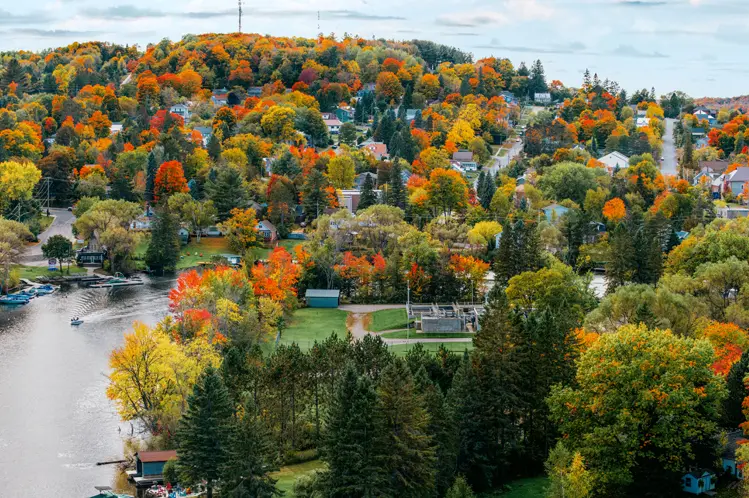 Luftaufnahme von Huntsville, Ontario, mit buntem Herbstlaub rund um den Fluss und der zwischen sanften Hügeln eingebetteten Stadt.